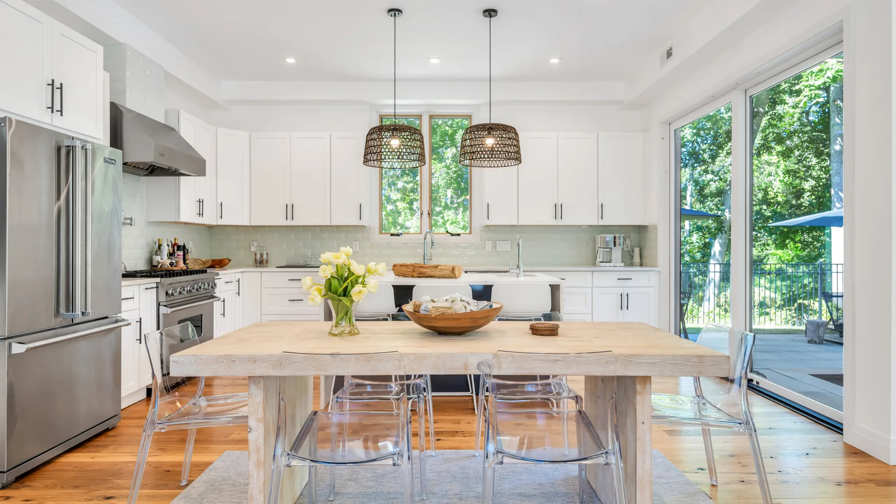 A bright kitchen with white cabinetry and a long wooden dining table.