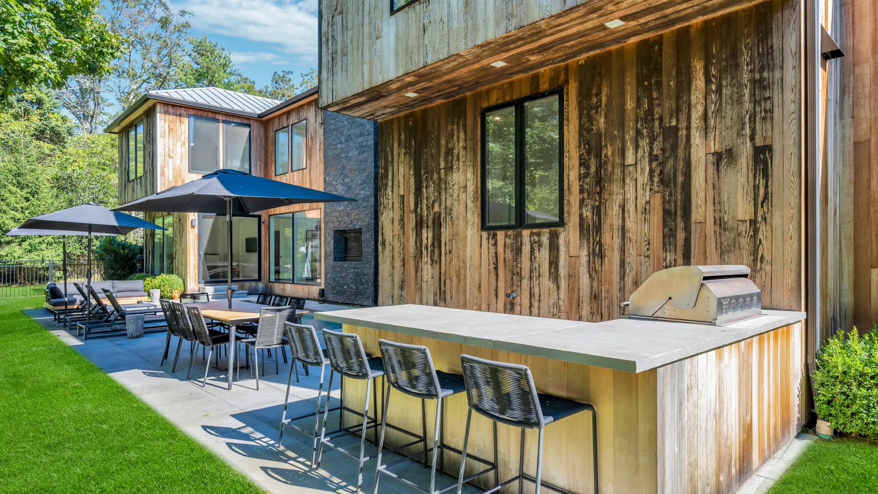Una zona de comedor al aire libre junto a un edificio de madera, con una barra larga y asientos.