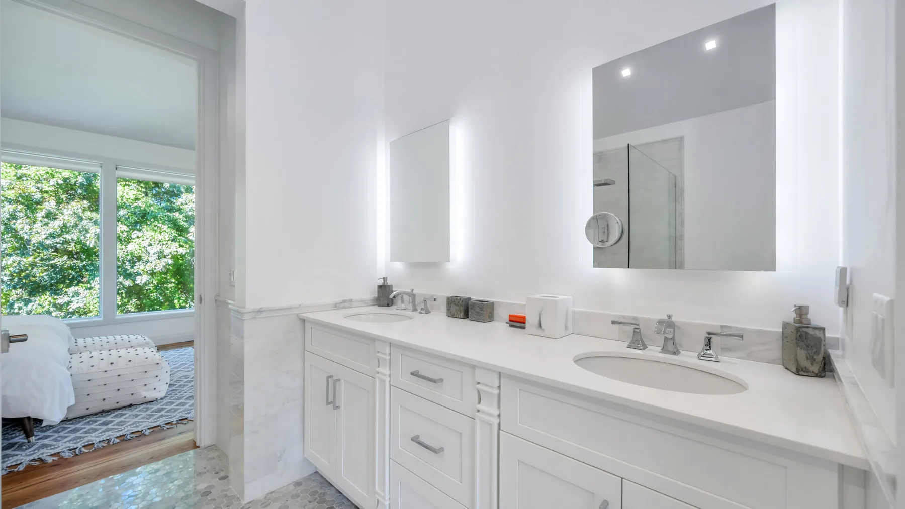 A bright bathroom vanity with a wide mirror and a doorway to a bedroom.
