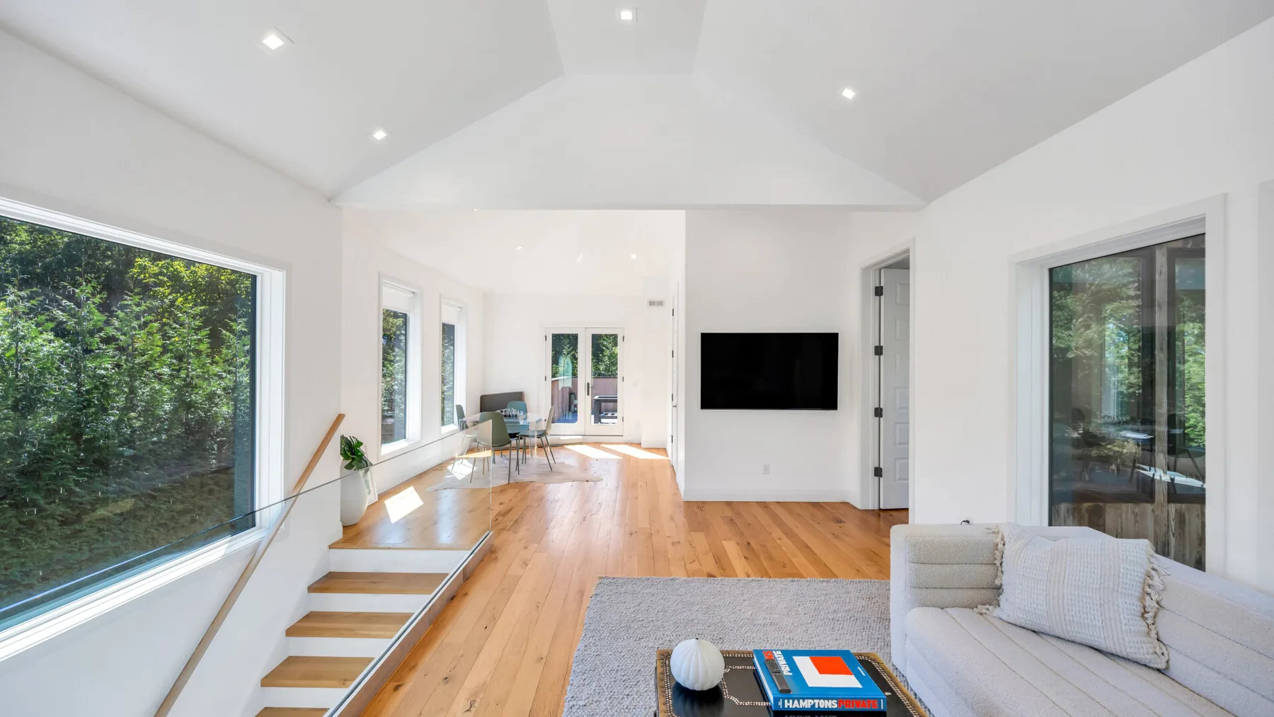 A bright living room with wood flooring, a television, and large windows.