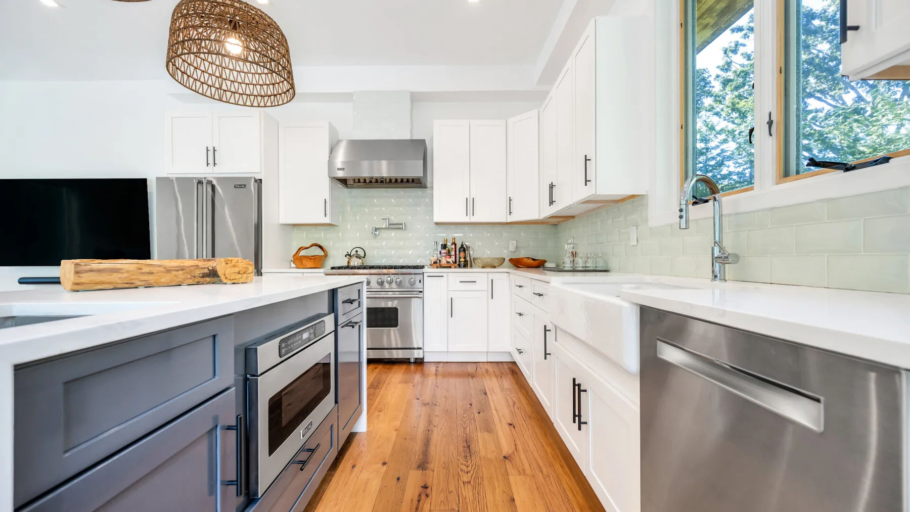 A bright kitchen with white cabinets, stainless steel appliances, and a wooden floor.