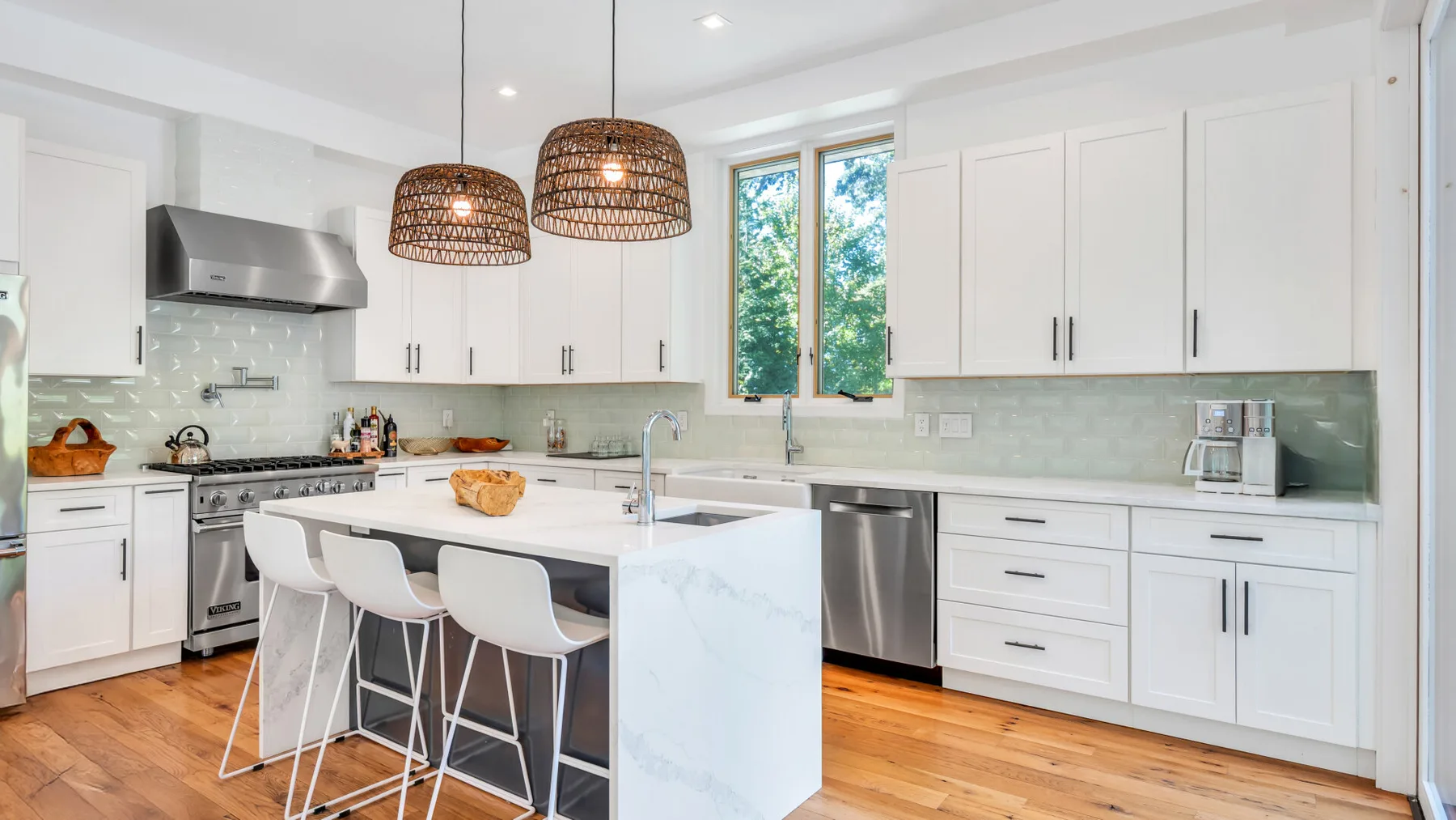 A bright kitchen with a central island, pendant lights, and large windows.