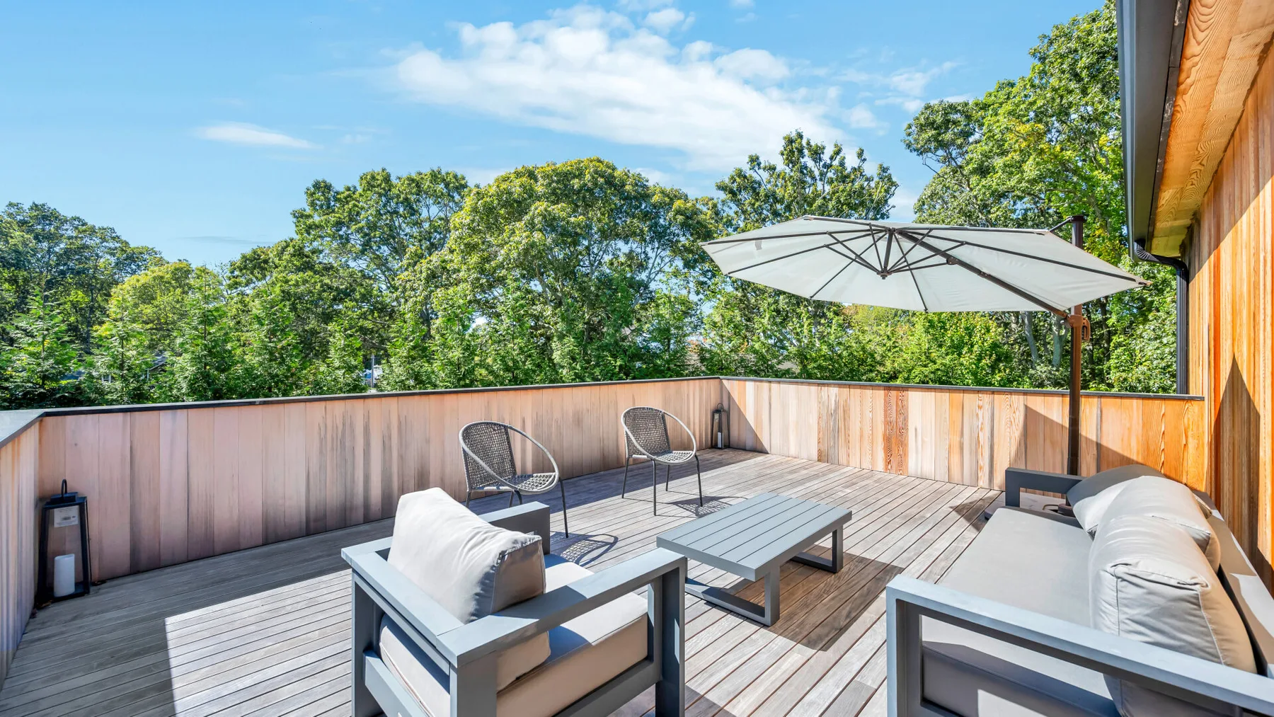 A sunny wooden deck has outdoor seating and a large open umbrella.