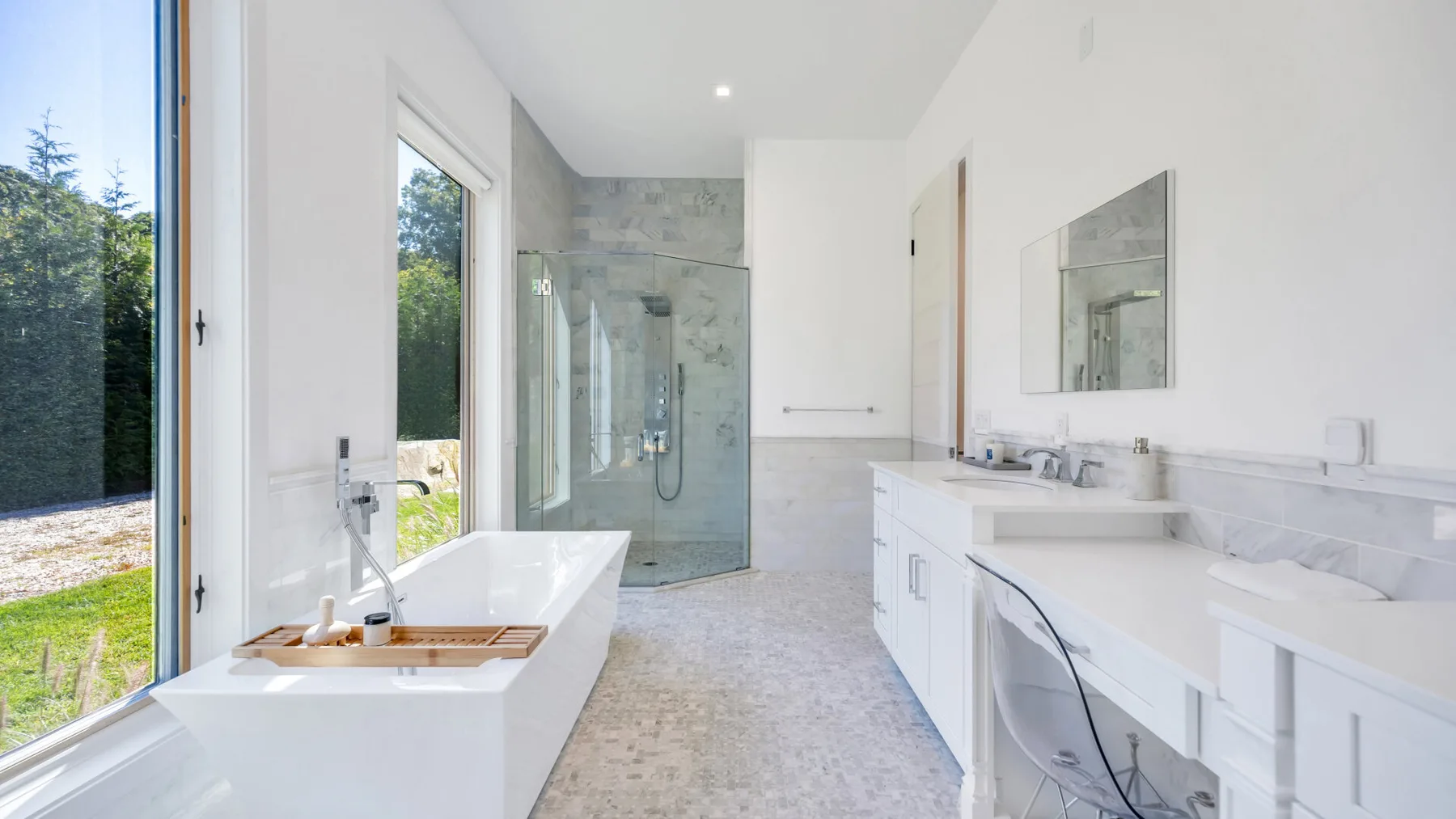 A bright bathroom with a freestanding bathtub, glass shower, and long vanity.