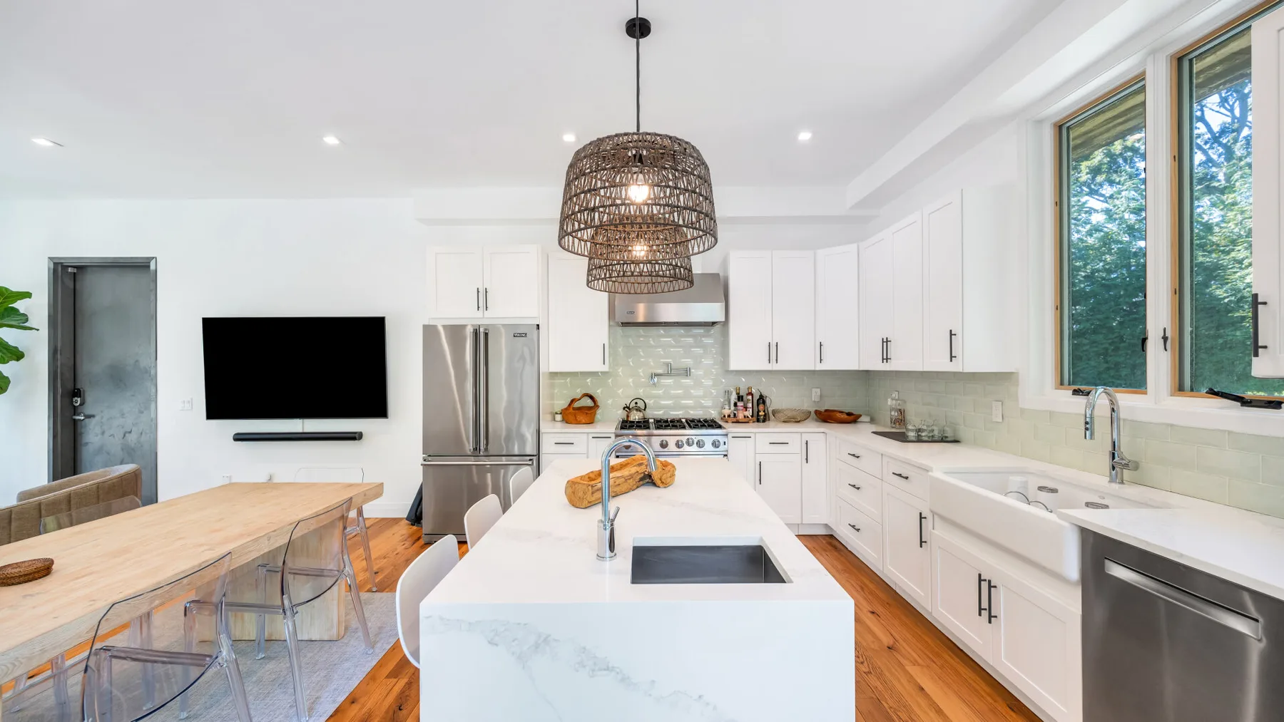 A bright modern kitchen has white cabinetry, a central island, and large windows.