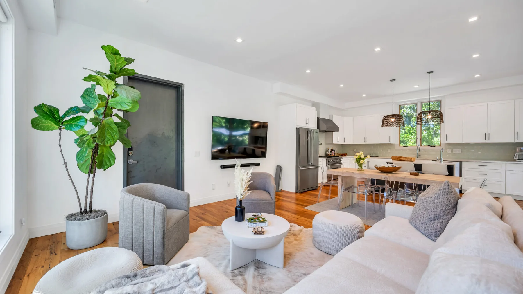An open-plan living room and kitchen with light seating and a dining table.