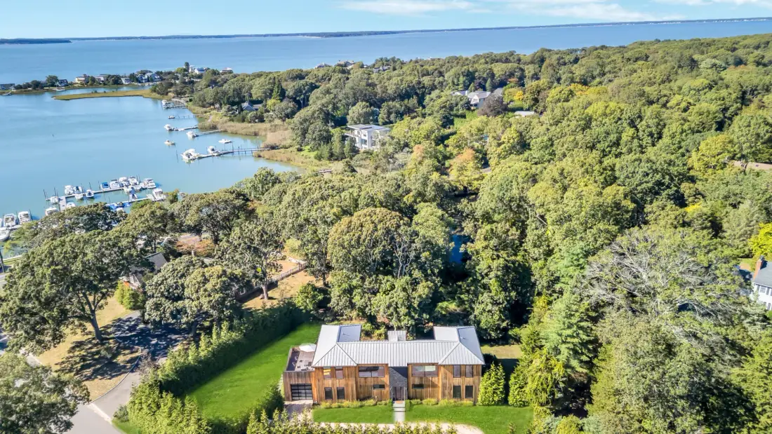 Aerial view of a house amid wooded greenery beside a broad waterway.