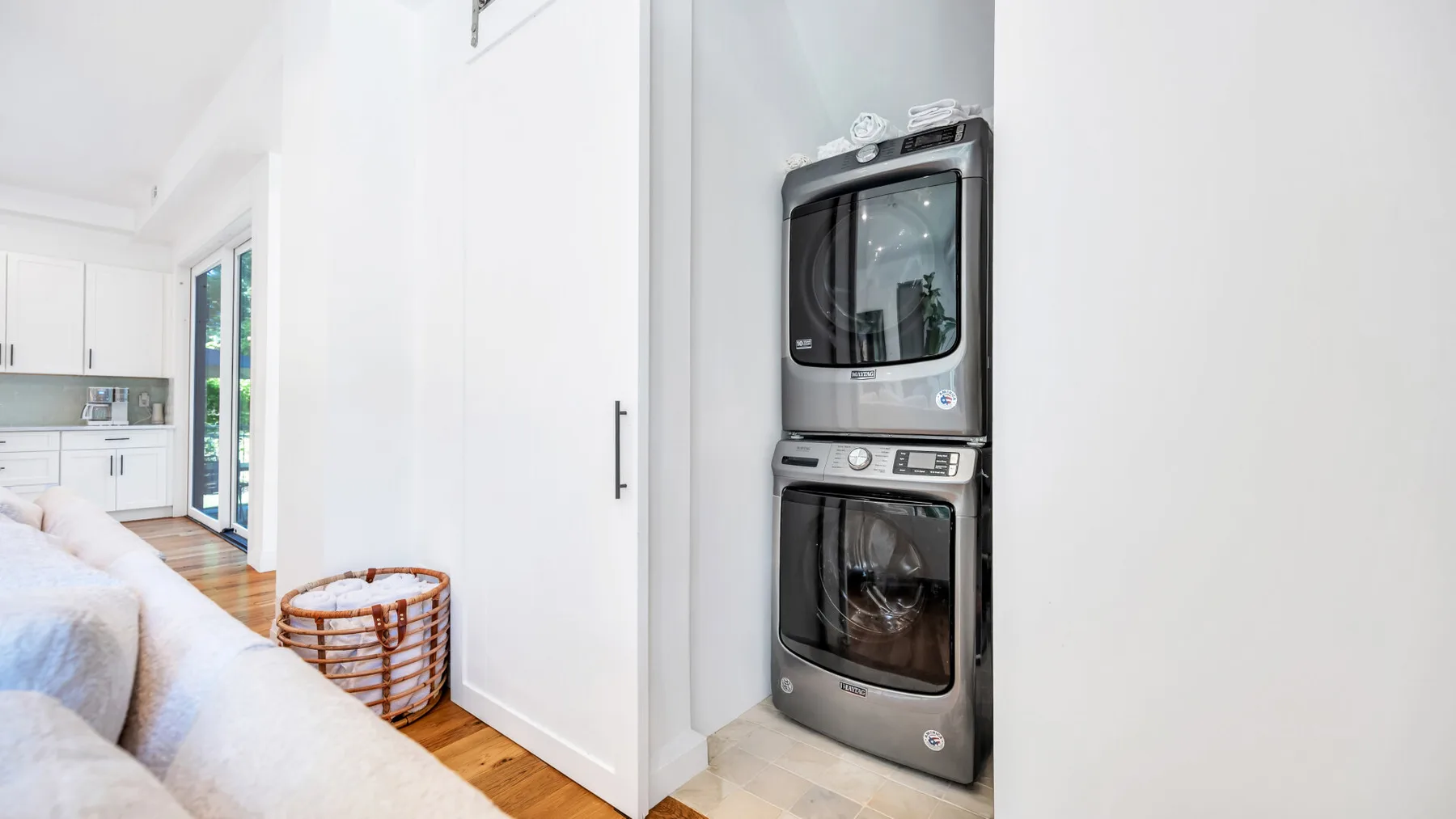A bright bedroom with a stacked washer and dryer beside the bed.
