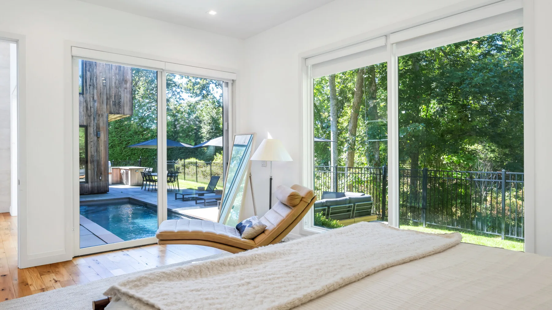 A bright bedroom opens onto a poolside patio through large glass doors.