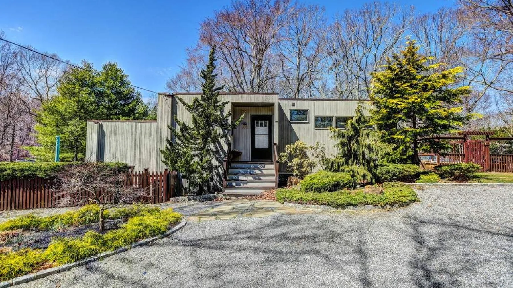 A low, modern home stands beside a paved driveway and landscaped garden.