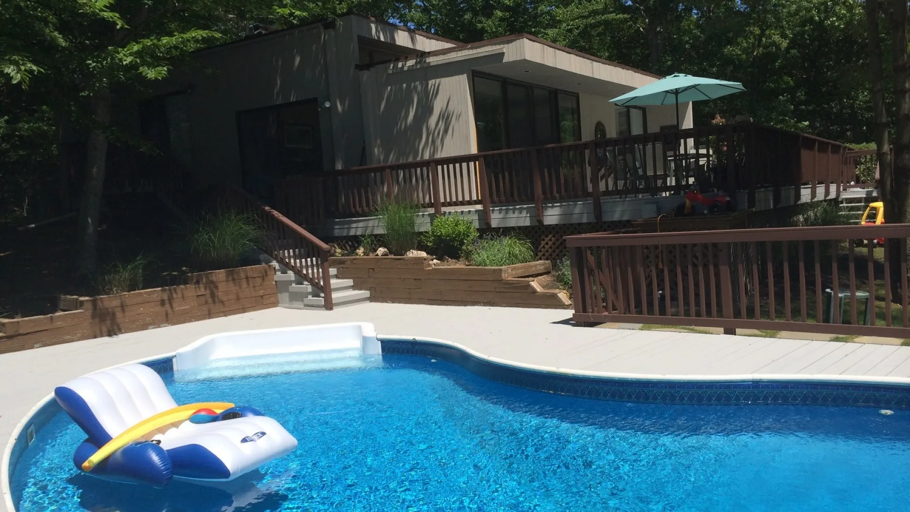 An outdoor swimming pool sits beside a raised deck with a shaded patio area.