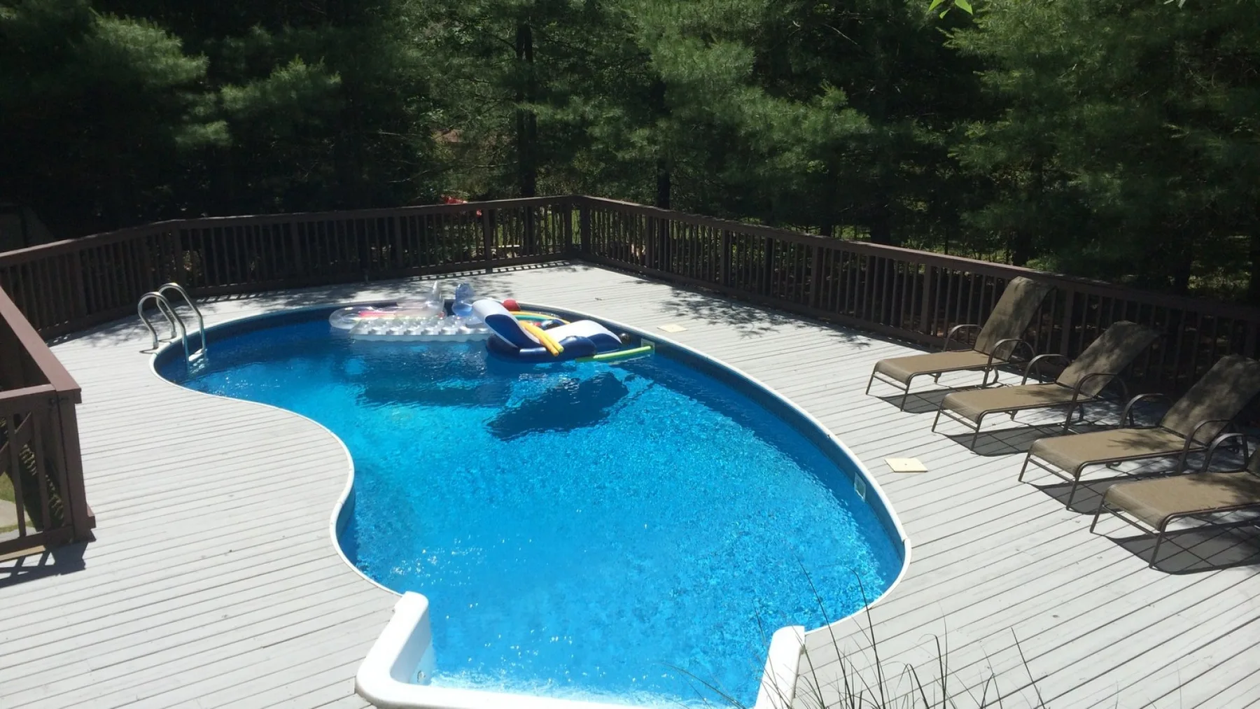 An outdoor swimming pool sits in a broad deck, with lounge seating along the side.
