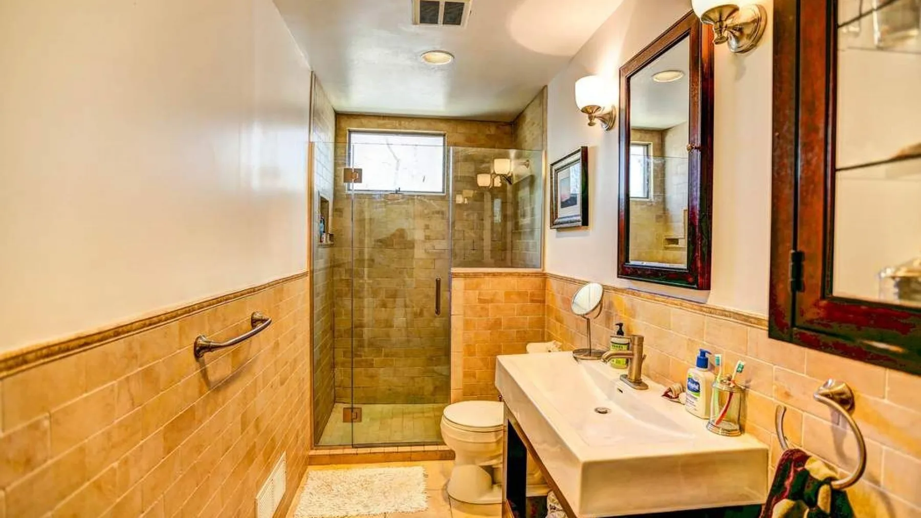 A bathroom with a glass shower, toilet, and long sink counter.