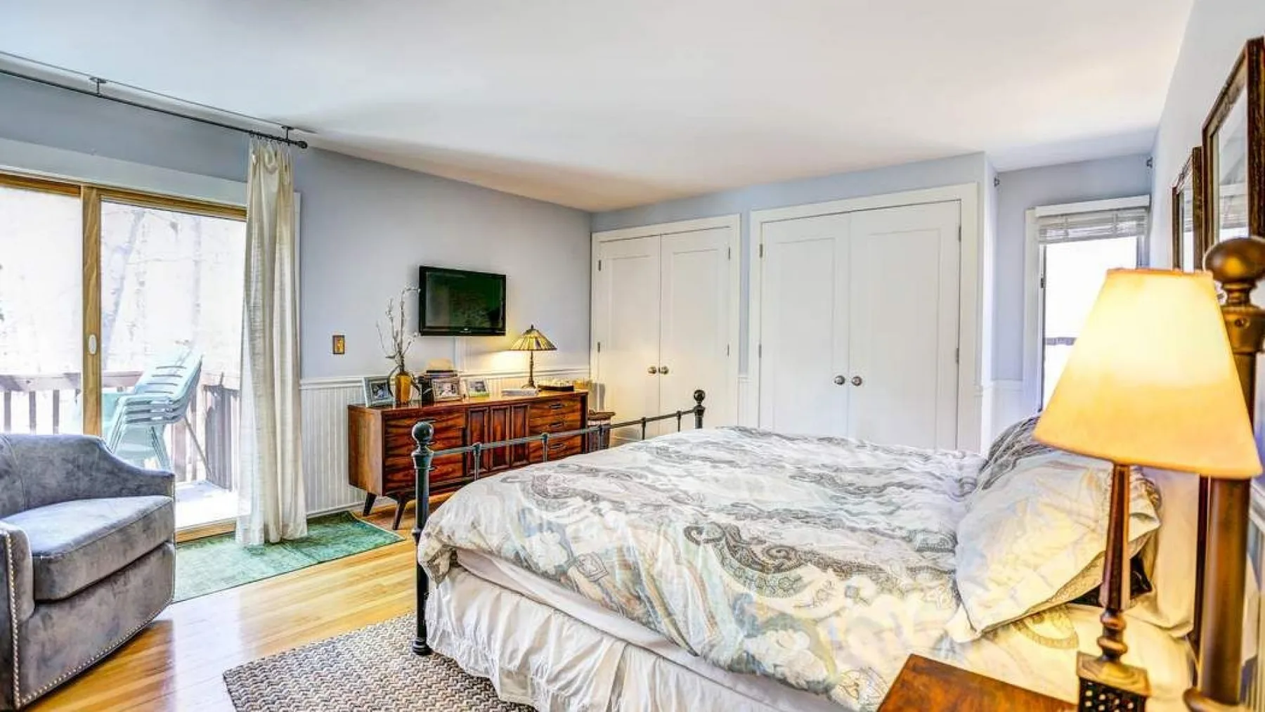 A bedroom with a large bed, a dresser, and a sliding glass door.