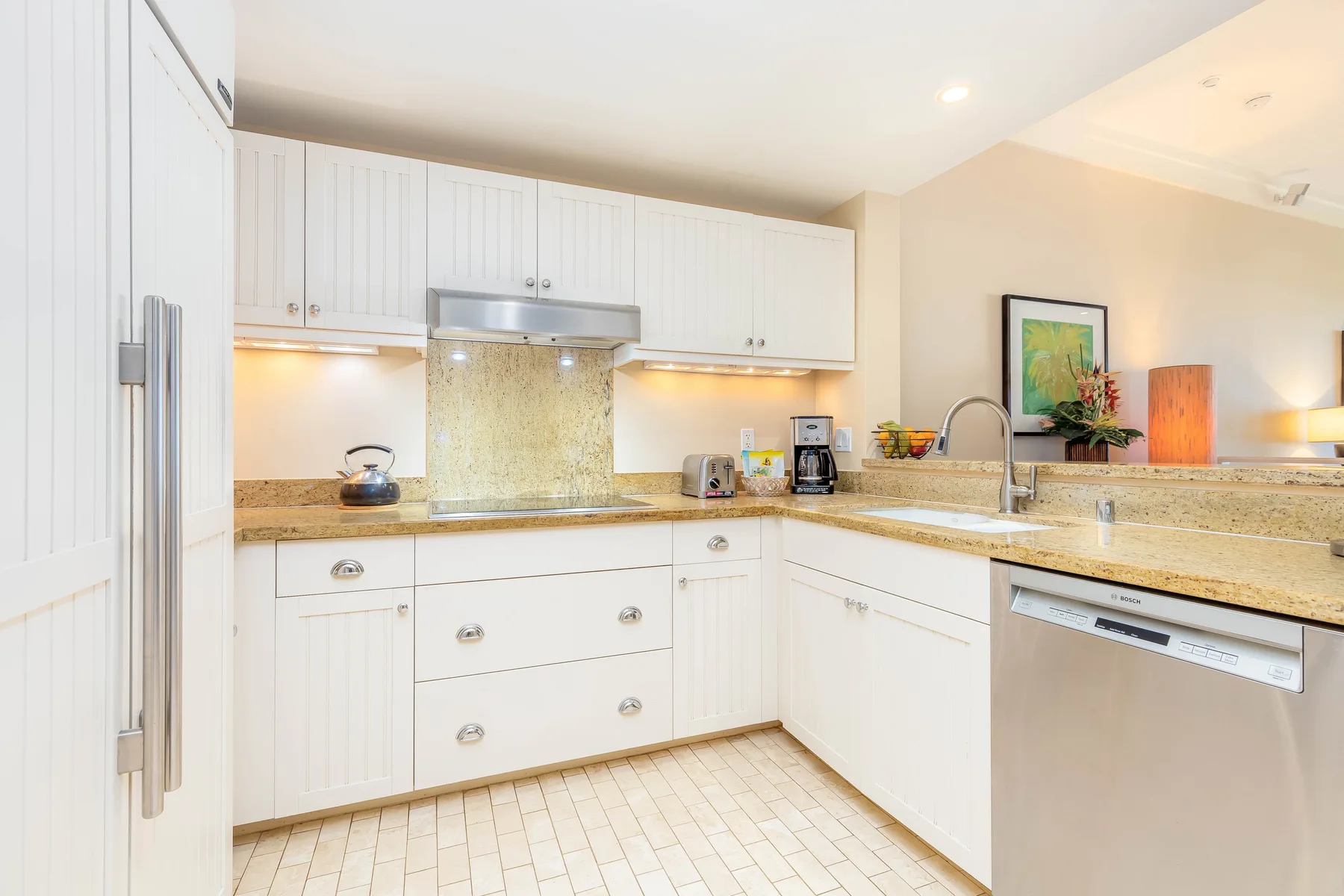 Una cocina luminosa con gabinetes blancos, encimeras de piedra y un lavavajillas de acero inoxidable.