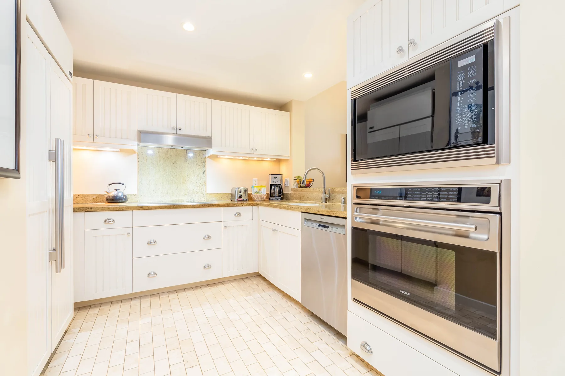 Una cocina luminosa con gabinetes blancos, salpicadero de azulejos y electrodomésticos integrados.