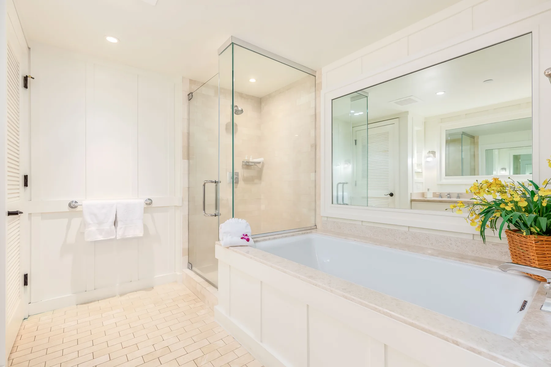 Un baño luminoso con ducha de cristal, bañera y espejo grande.