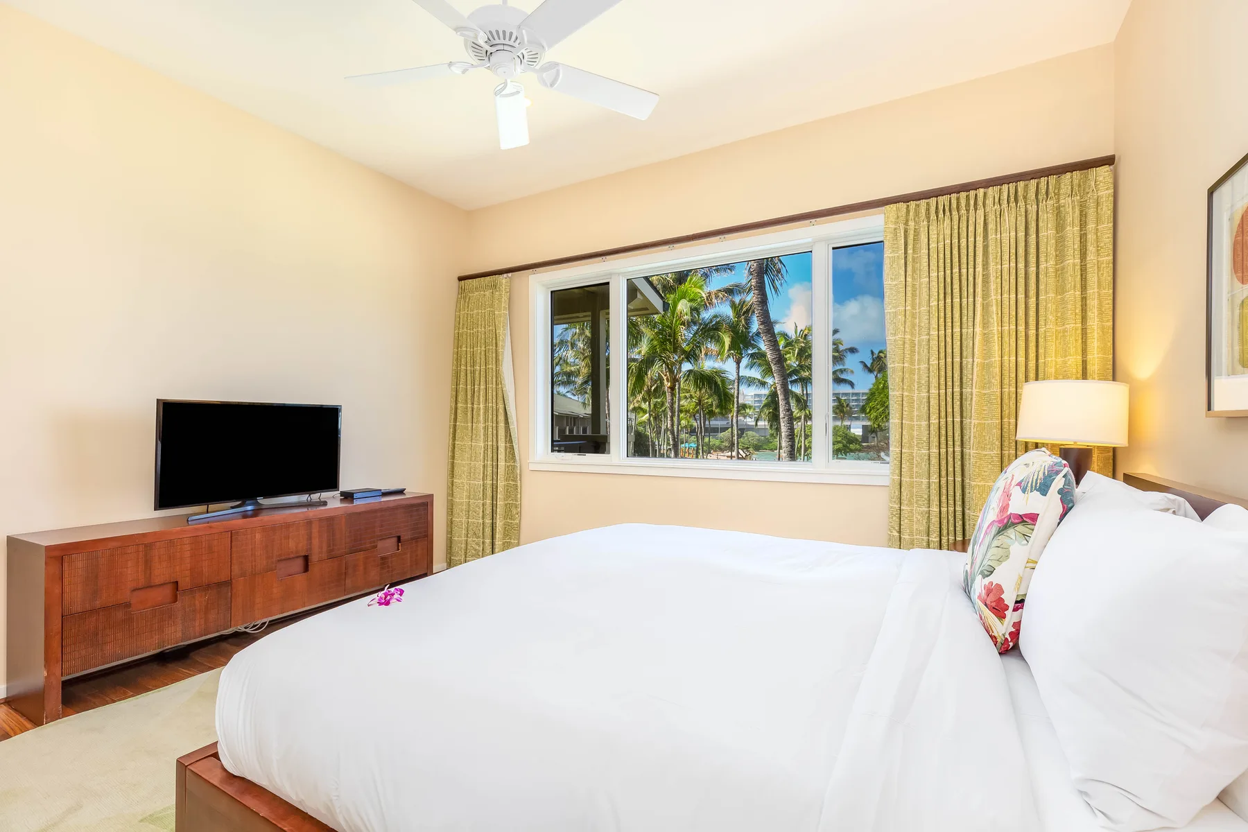Un dormitorio con una cama grande, un televisor y una ventana con vista a palmeras.