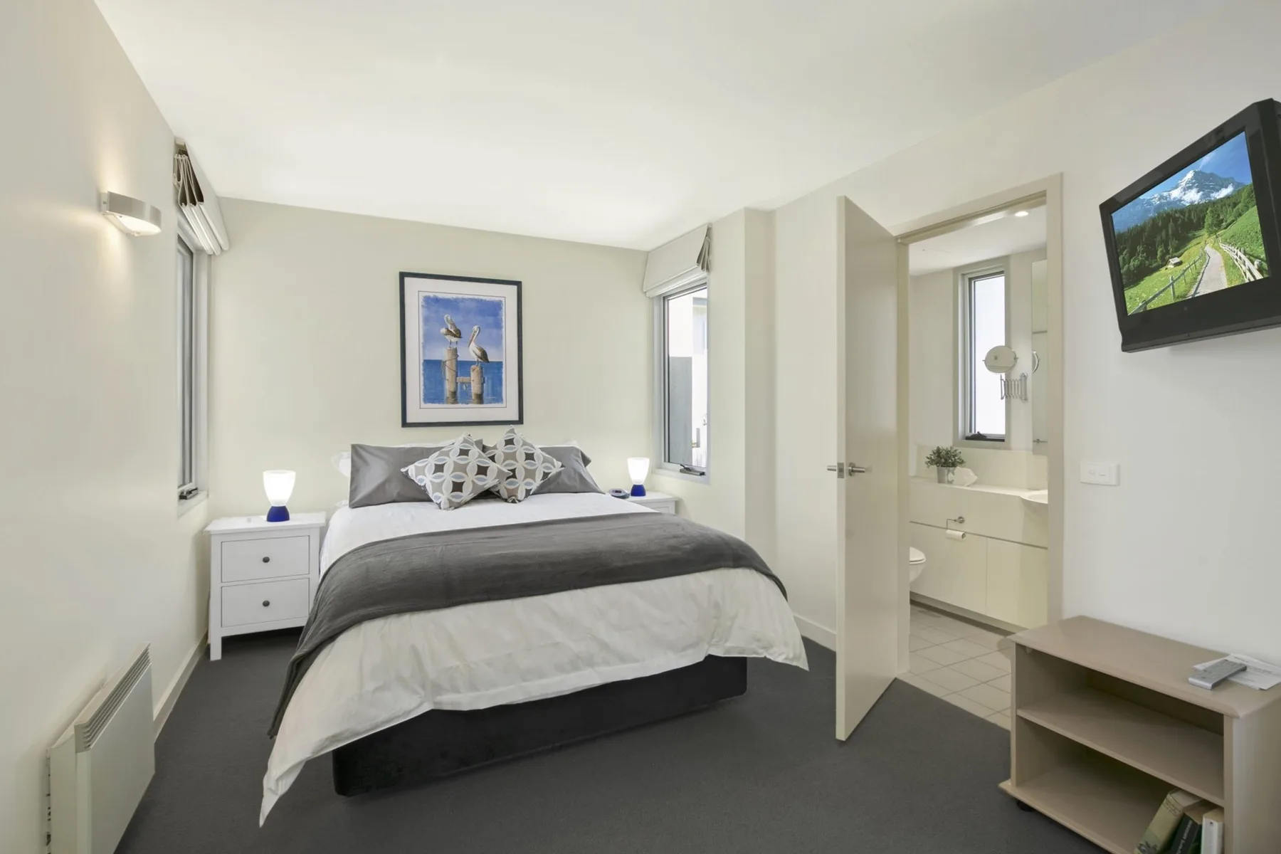 Un dormitorio con una cama, mesitas de noche y una puerta abierta al baño.
