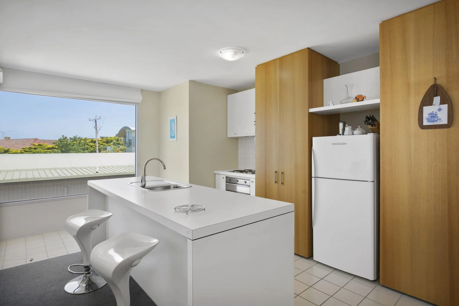 Cocina luminosa con isla blanca, refrigerador y una ventana grande.