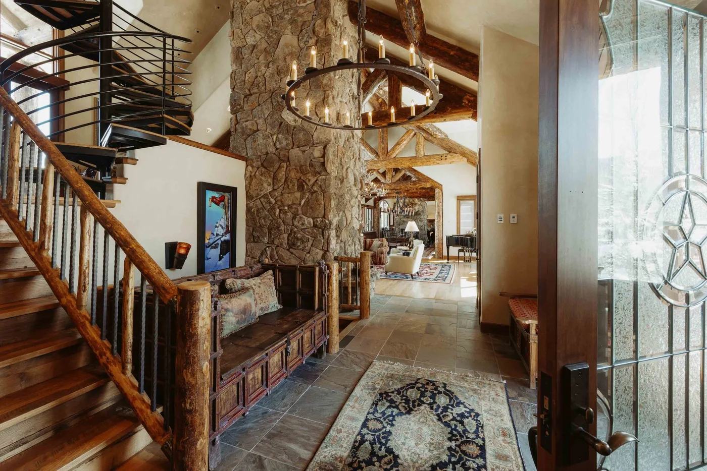 A rustic home entryway opens into a living area, with a staircase and stone wall.