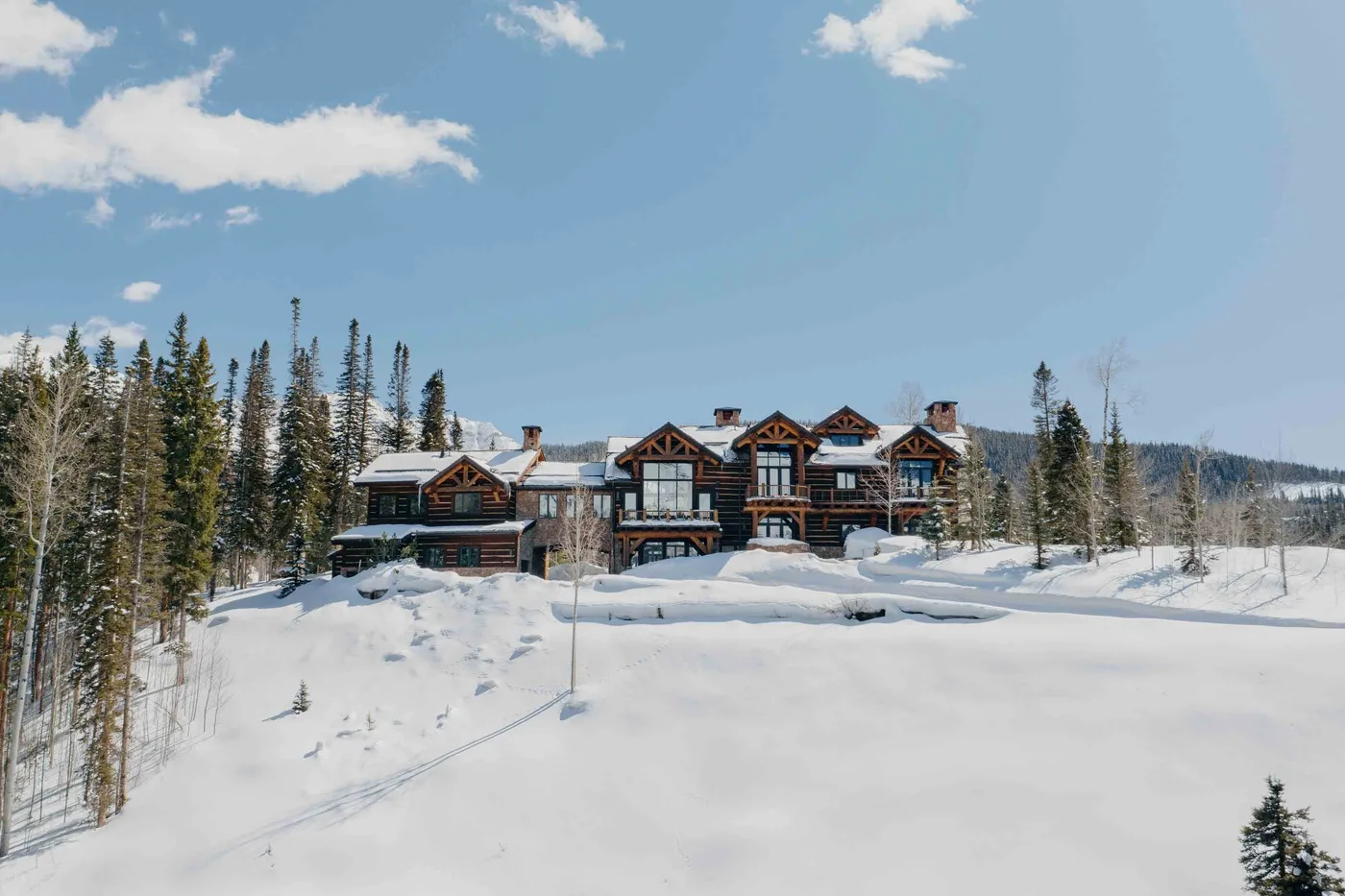 A large lodge stands in a snowy clearing among evergreen trees.