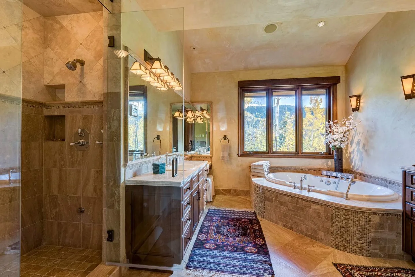 A bathroom with a glass-enclosed shower, vanity, and bathtub beside a window.