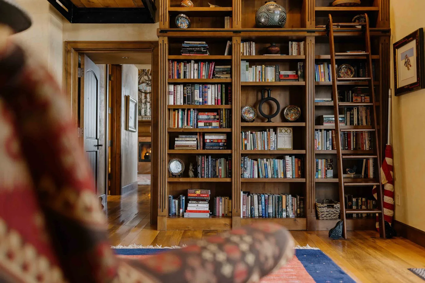 A warmly lit library with floor-to-ceiling bookshelves and a patterned rug.