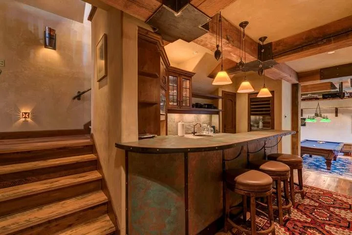 A warmly lit bar counter with stools sits beside a staircase and open lounge area.