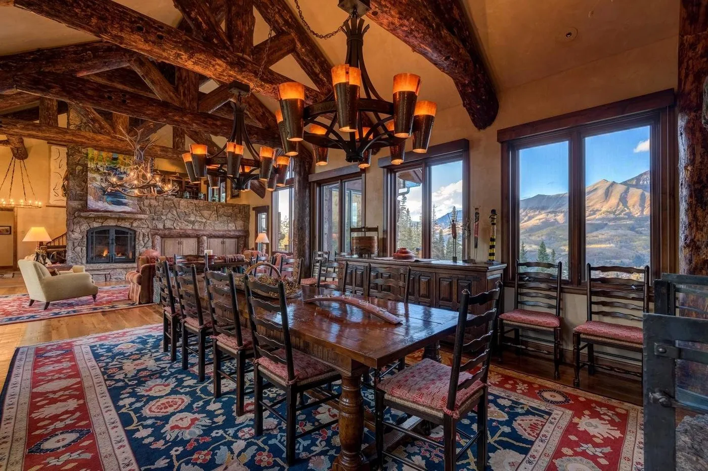 A dining room with a long wooden table and large windows overlooking mountains.