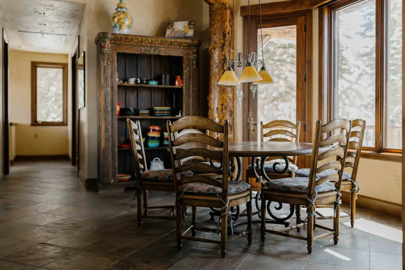 A dining area with a wooden table and chairs beside large windows.