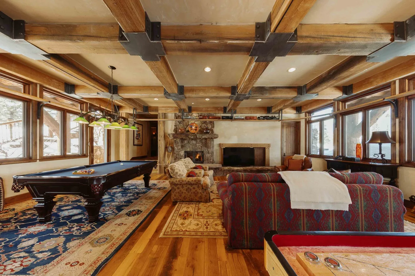 A rustic living room with a pool table, fireplace, and large windows.