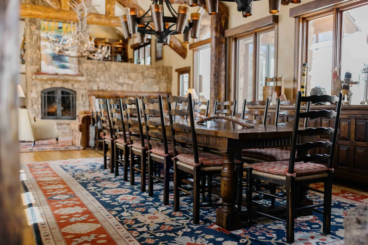 A dining room with a long wooden table and chairs beside large windows.
