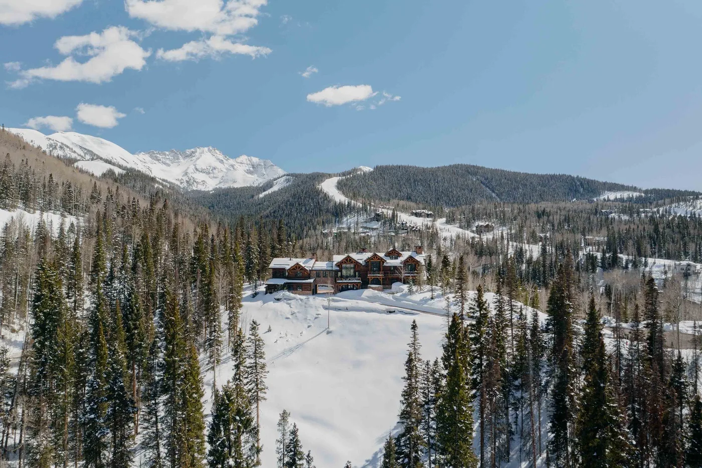 A cluster of buildings sits in a snowy mountain landscape among evergreen trees.