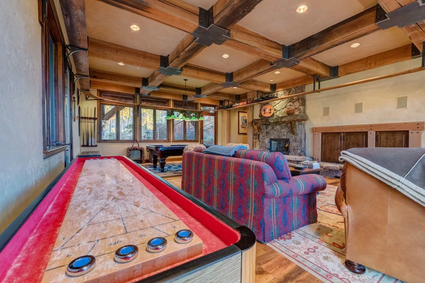 A rustic game room with a pool table, colorful seating, and a stone fireplace.