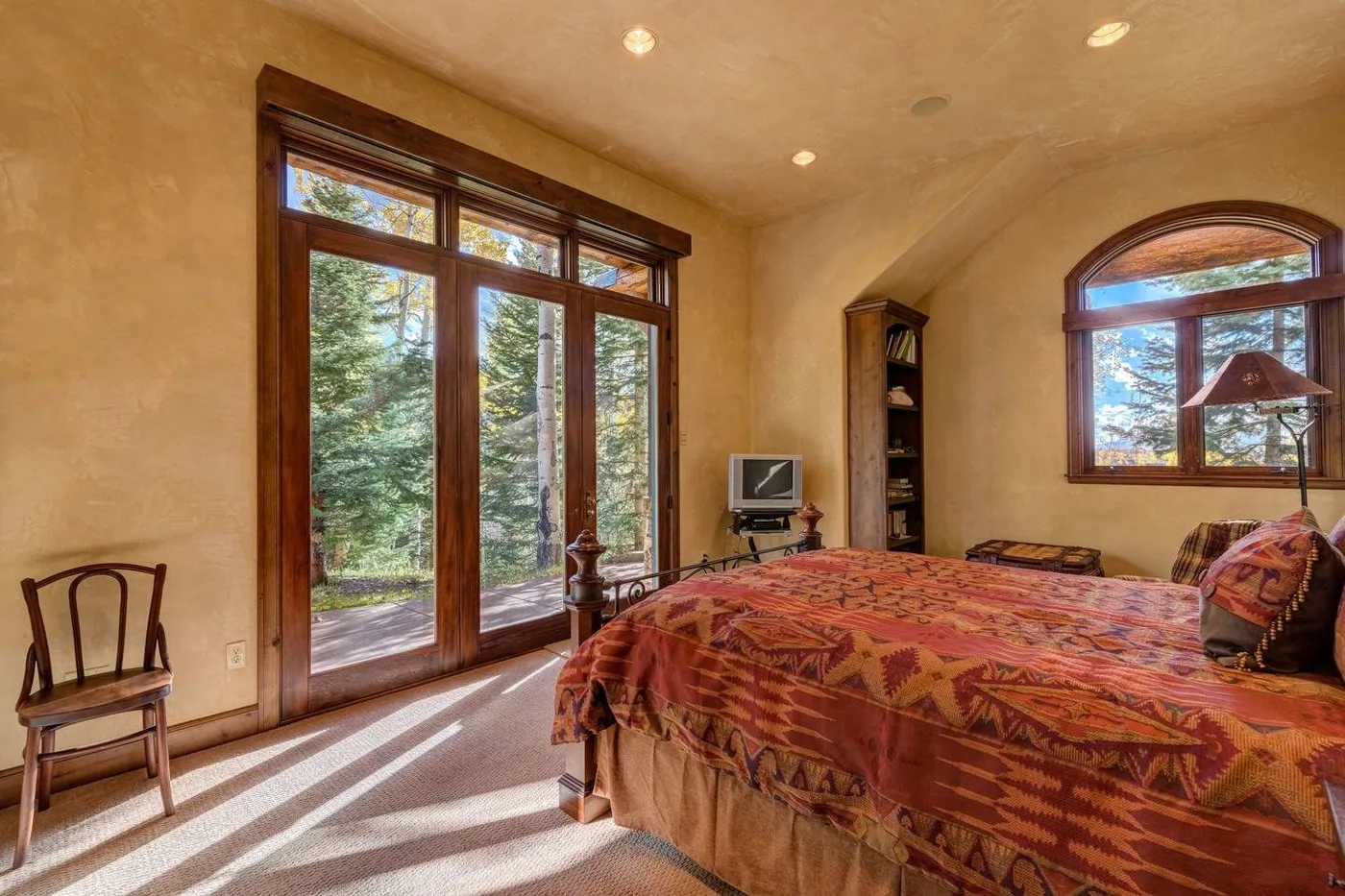 A bedroom with a large bed and tall windows overlooking trees.