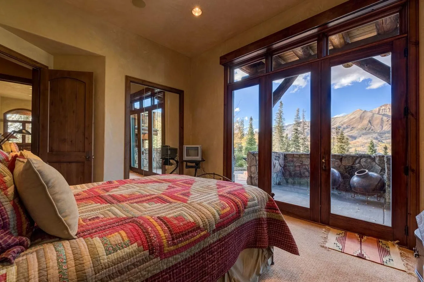 A bedroom with a colorful bedspread and large glass doors opening onto mountain views.