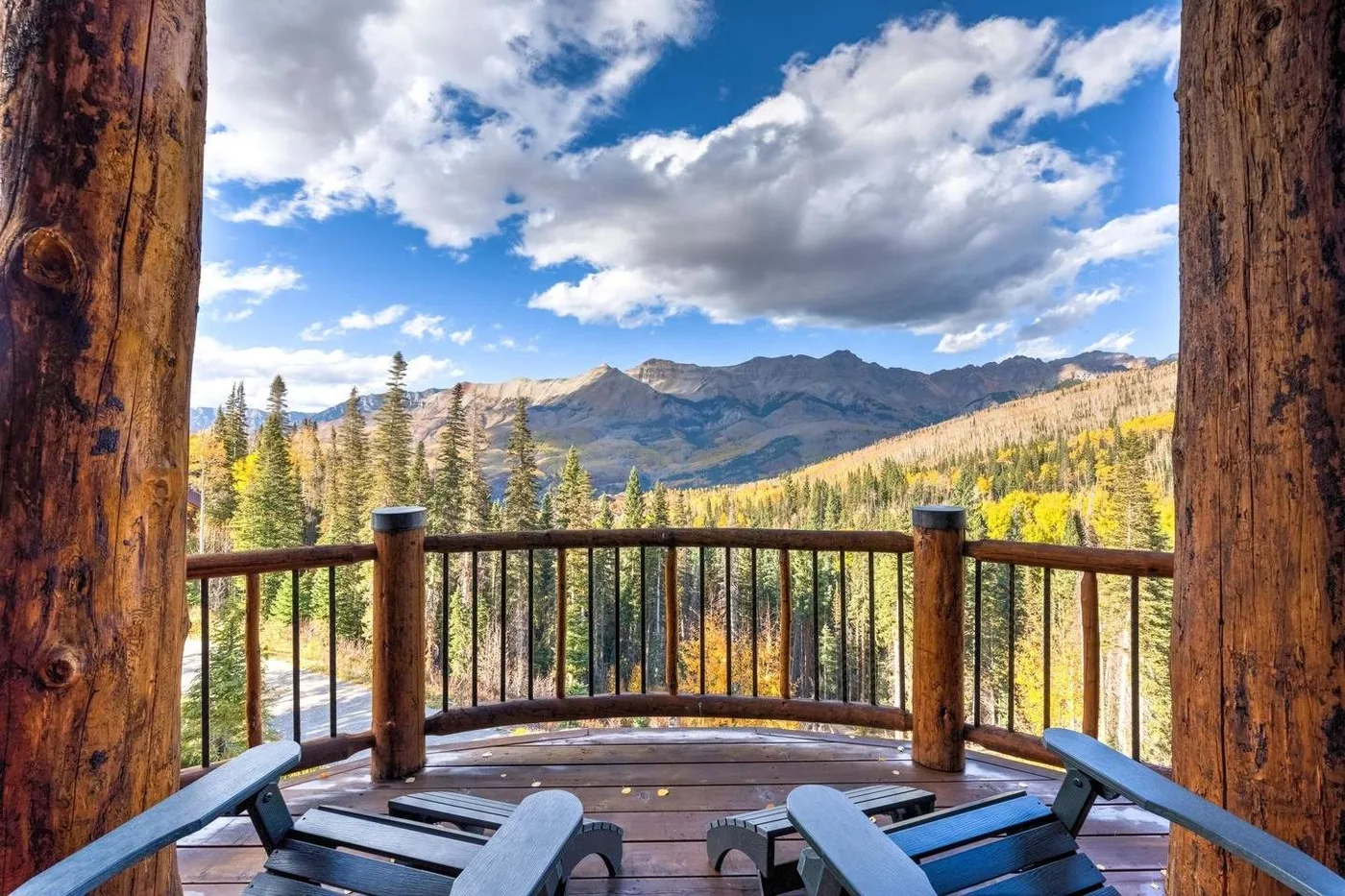 A wooden balcony overlooks a mountain valley beneath a cloudy blue sky.