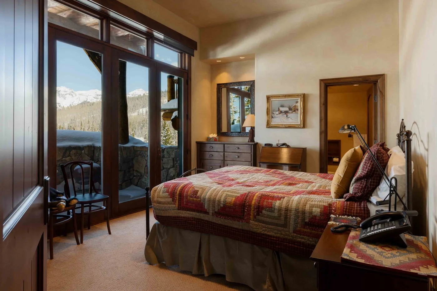 A bedroom with a bed beside tall glass doors and a mountain view.