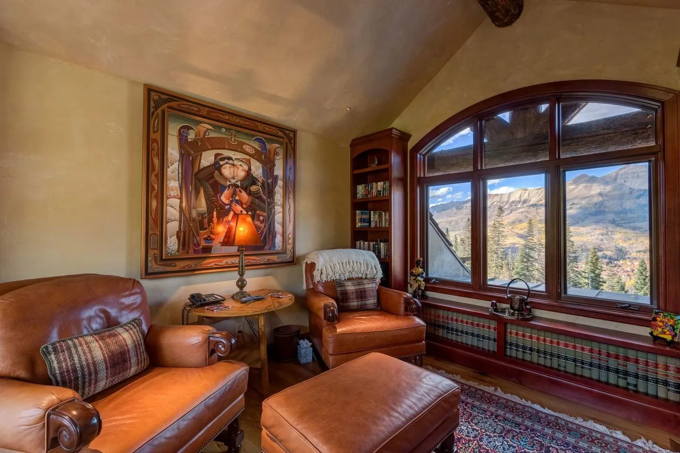 A sitting room with leather seating, a large arched window, and mountain views.