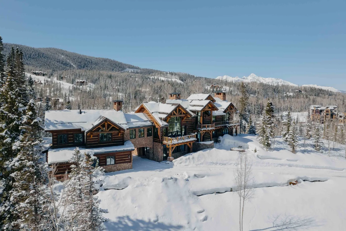 Snow-covered mountain lodge surrounded by pine trees and a winter landscape.