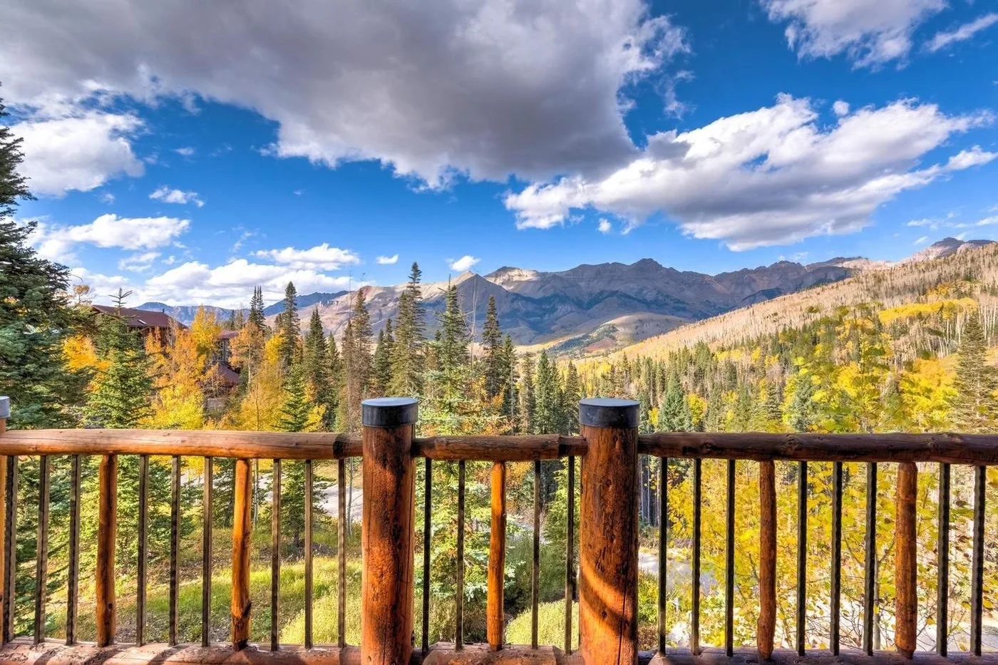 Mountain scenery with autumn-colored trees viewed from a wooden deck railing.