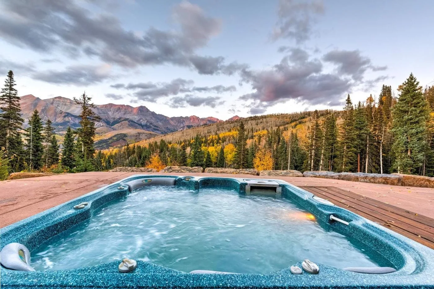 An outdoor hot tub overlooks a forested mountain landscape.