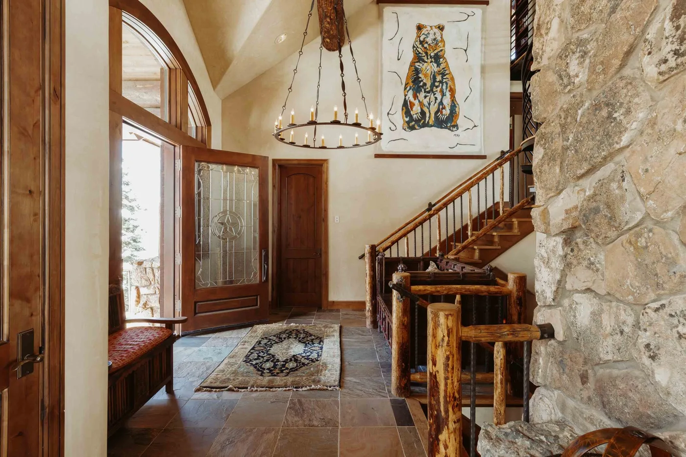 A rustic entry hall features a staircase, stone wall, and arched windows.