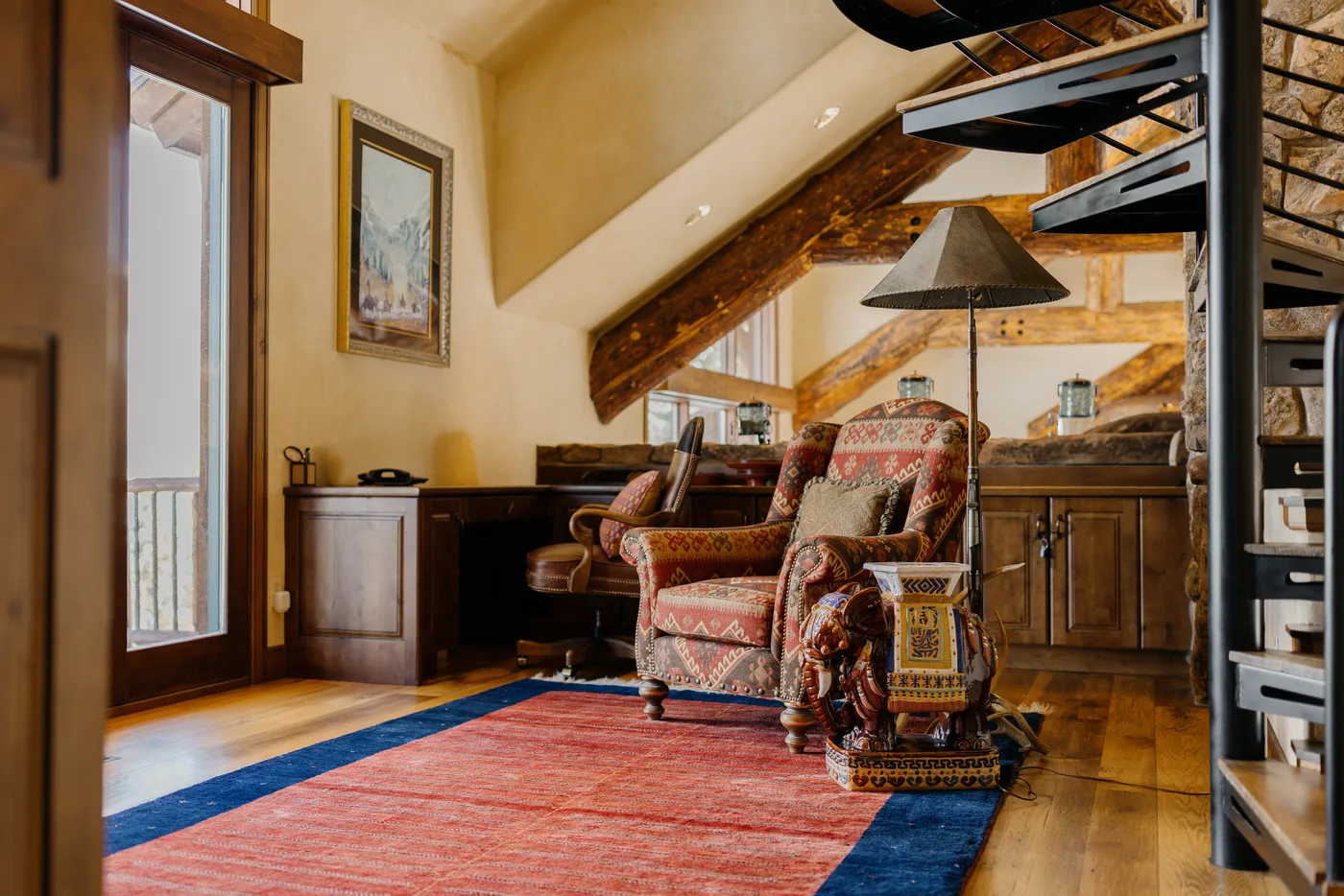 A warmly furnished living area with patterned seating, a rug, and exposed wooden beams.