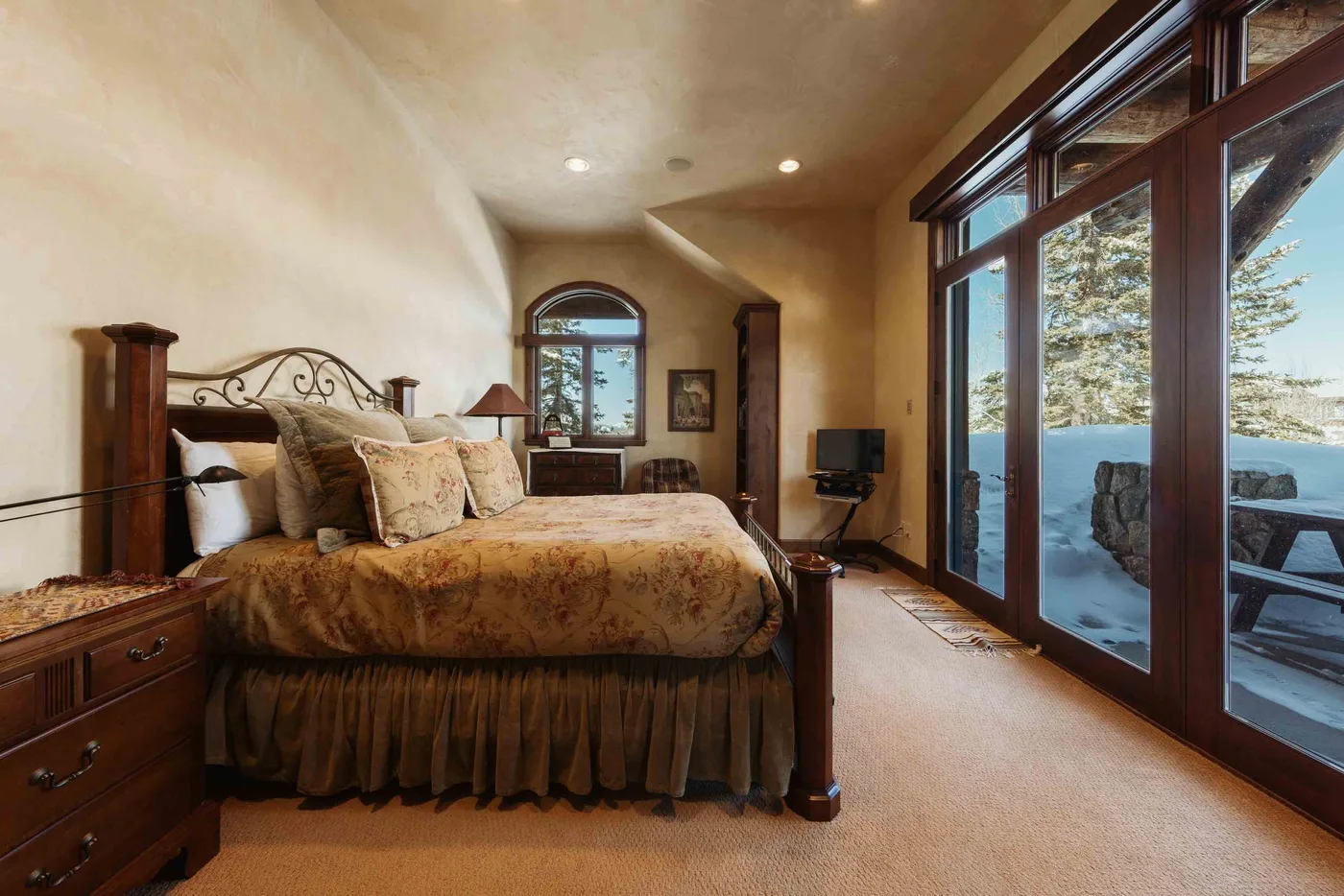 A bedroom with a large bed beside tall windows overlooking a lake.