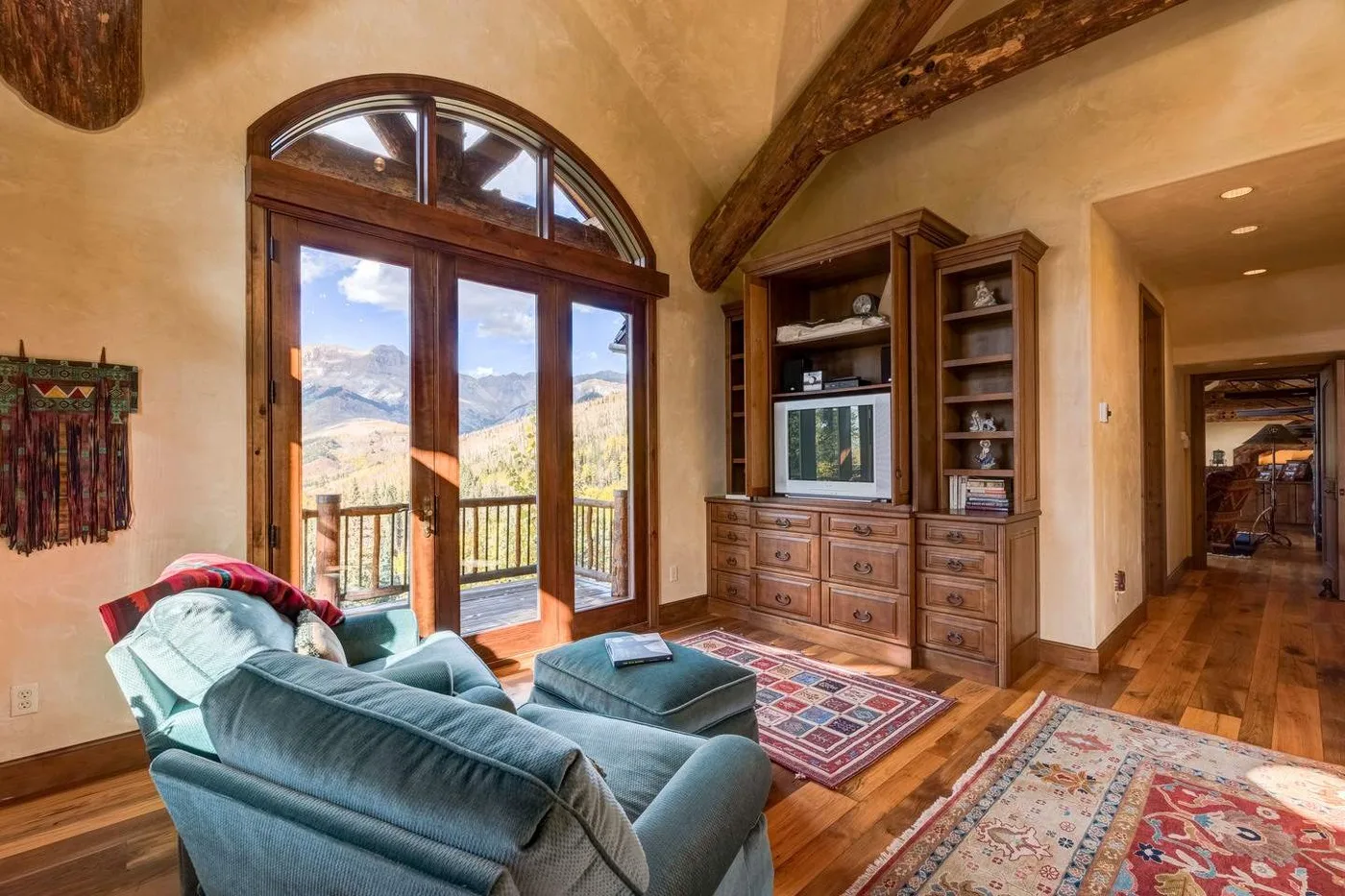 A living room with seating, a television, and arched glass doors opening onto a mountain view.