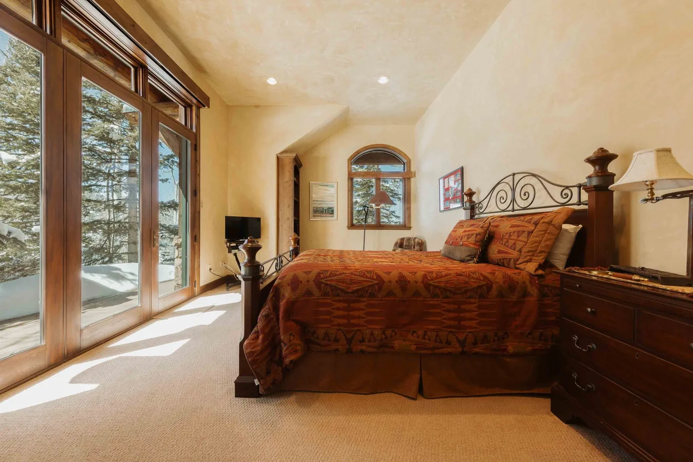 A bedroom with a large bed beside tall windows overlooking a snowy landscape.