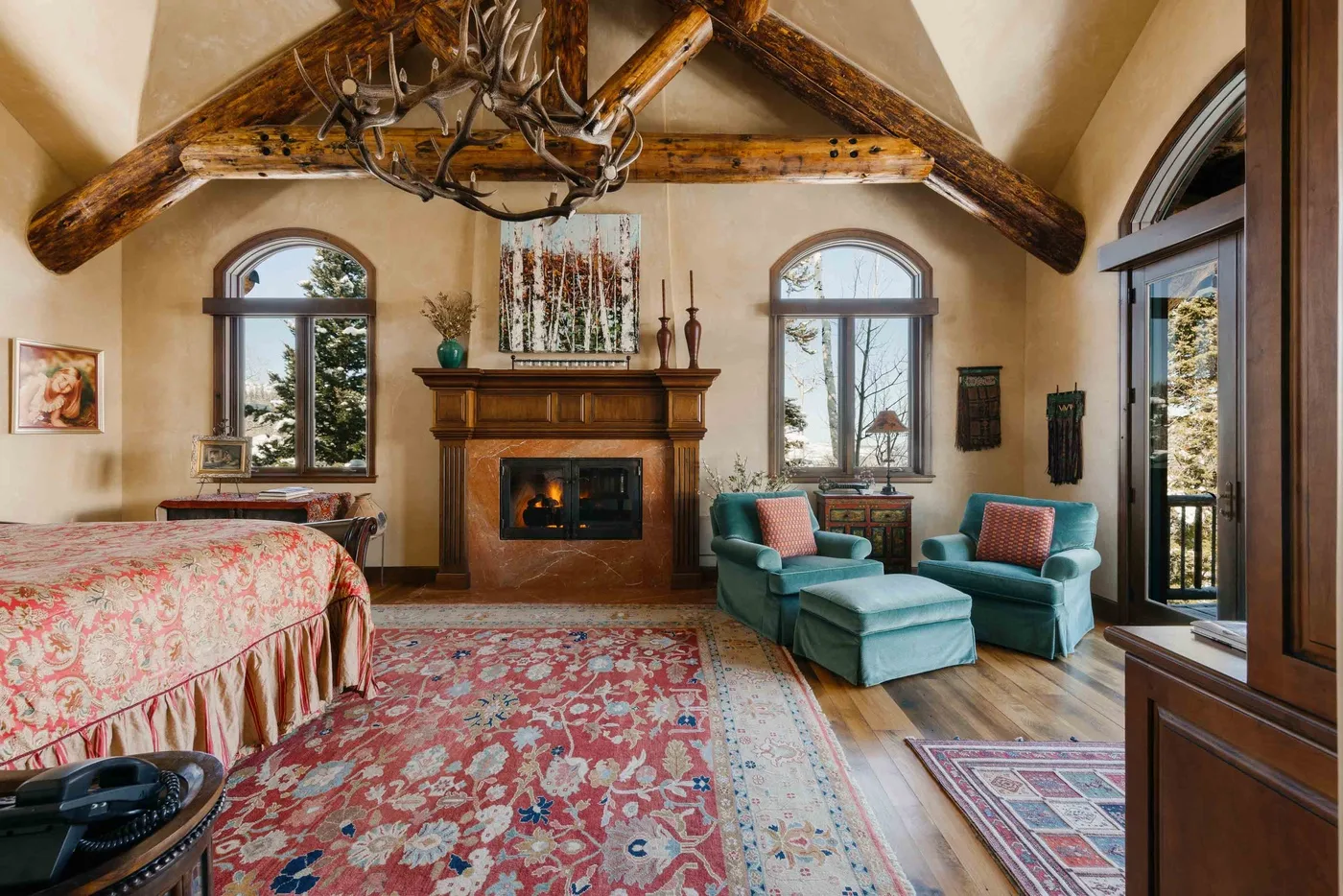 A bedroom seating area with a fireplace, teal armchairs, and a patterned rug.
