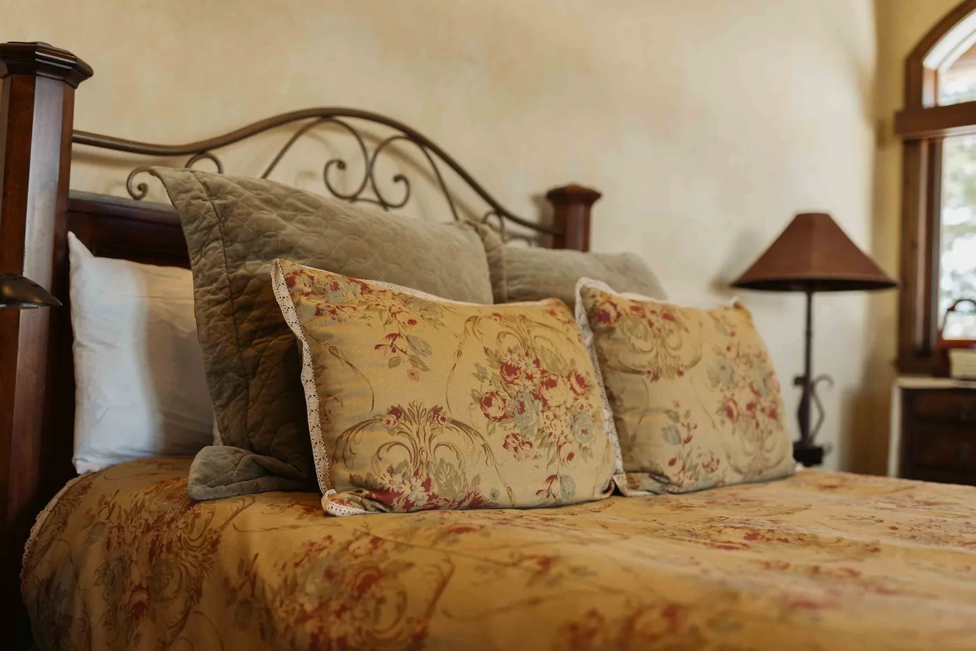 A bedroom with a made bed, patterned pillows, and a bedside lamp.